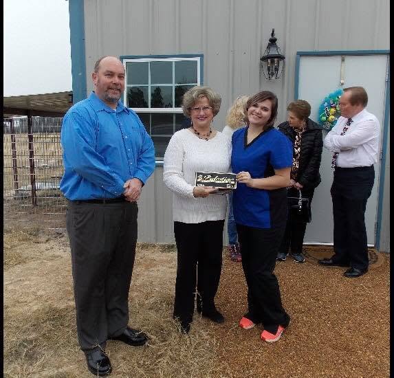 Two women holding a plaque pose with a man in front of a building, with two others visible in the background