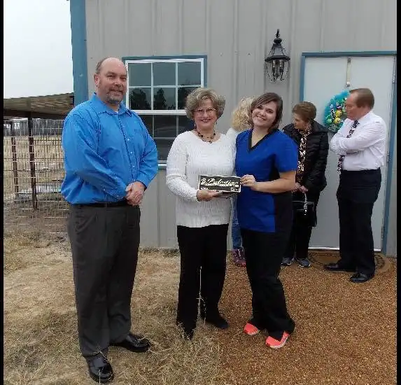 Two women holding a plaque pose with a man in front of a building, with two others visible in the background